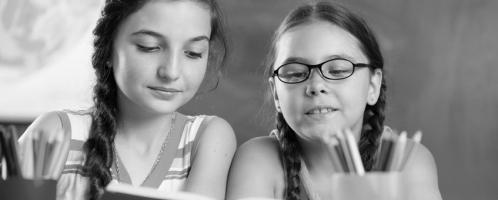 twee meisjes lezen samen in een boek in de klas