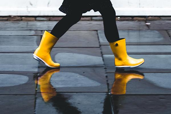 vrouw loopt in gele regenlaarzen weerspiegelend op de natte stoep